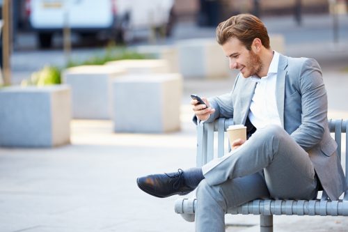 Businessman On Park Bench With Coffee Using Mobile Phone