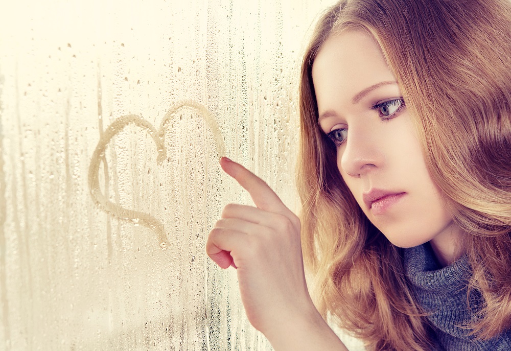 sad enamored girl draws a heart on the window in the rain